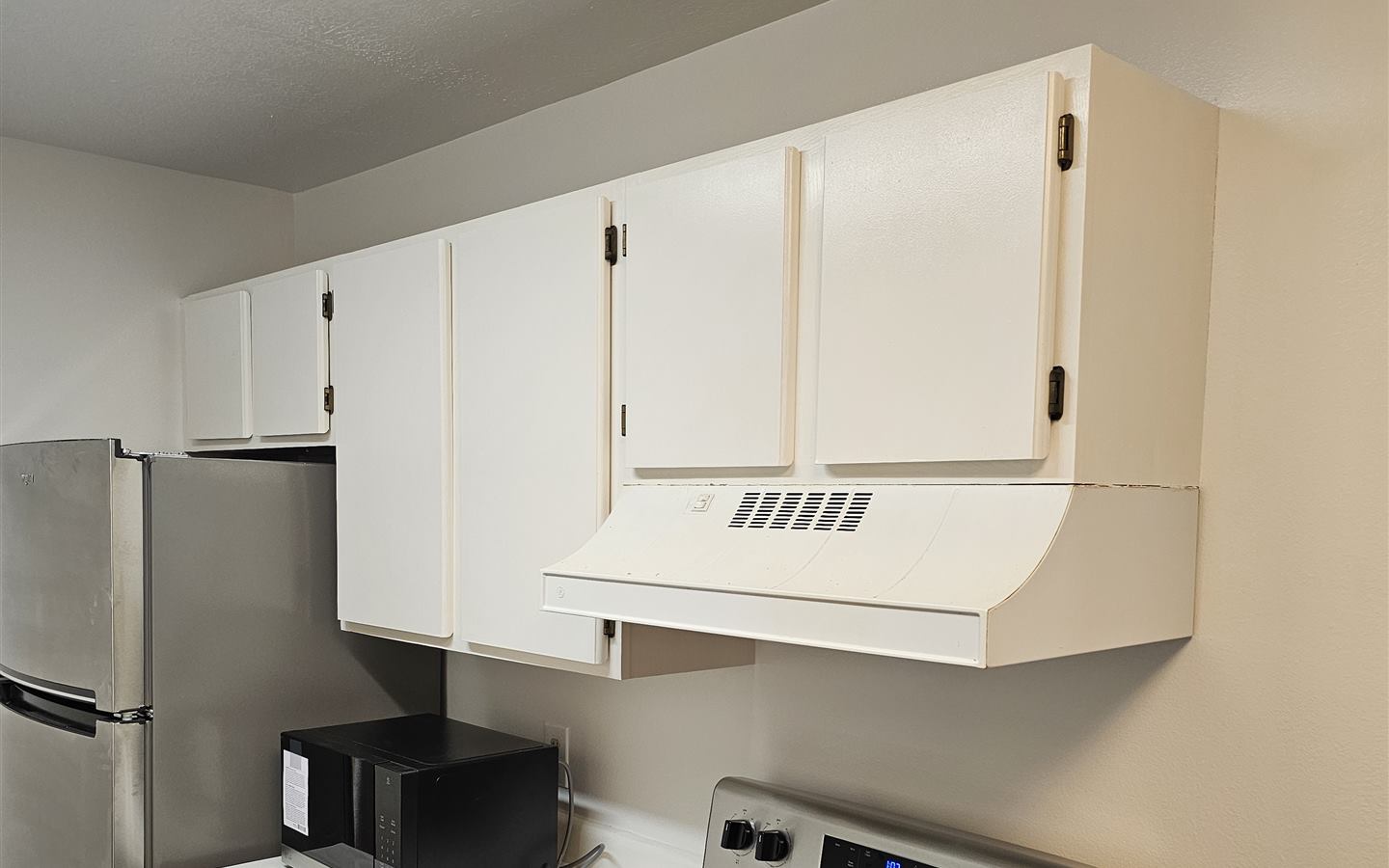 Refreshed kitchen with repainted white cabinets, range hood, and new stainless refrigerator